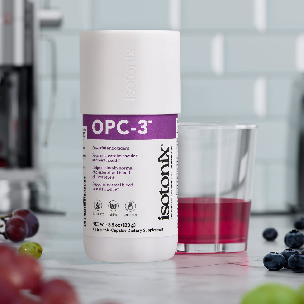 Isotonix OPC-3 bottle (new packaging) beside a glass of the antioxidant drink with grapes and blueberries on a kitchen counter