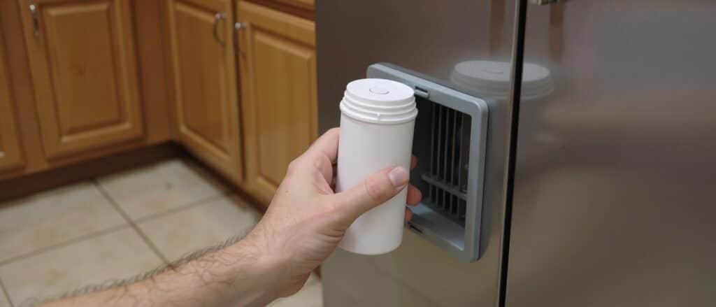 Installing a white refrigerator water filter cartridge into the base grille of a stainless-steel fridge